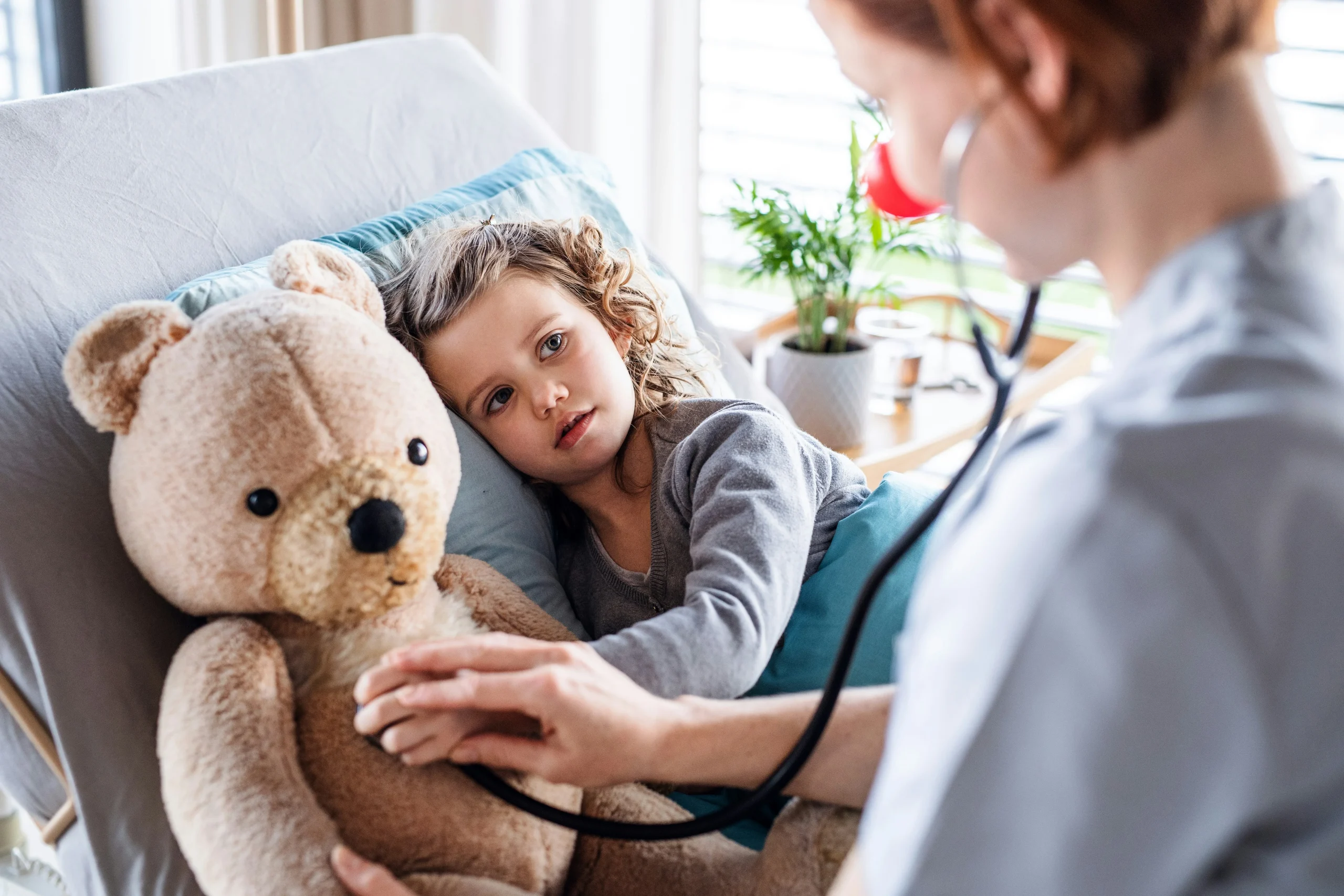A doctor using a stethoscope on a teddy bear while a young girl looks on, symbolizing the importance of a letter of intent for a special needs child in ensuring proper medical care and planning.