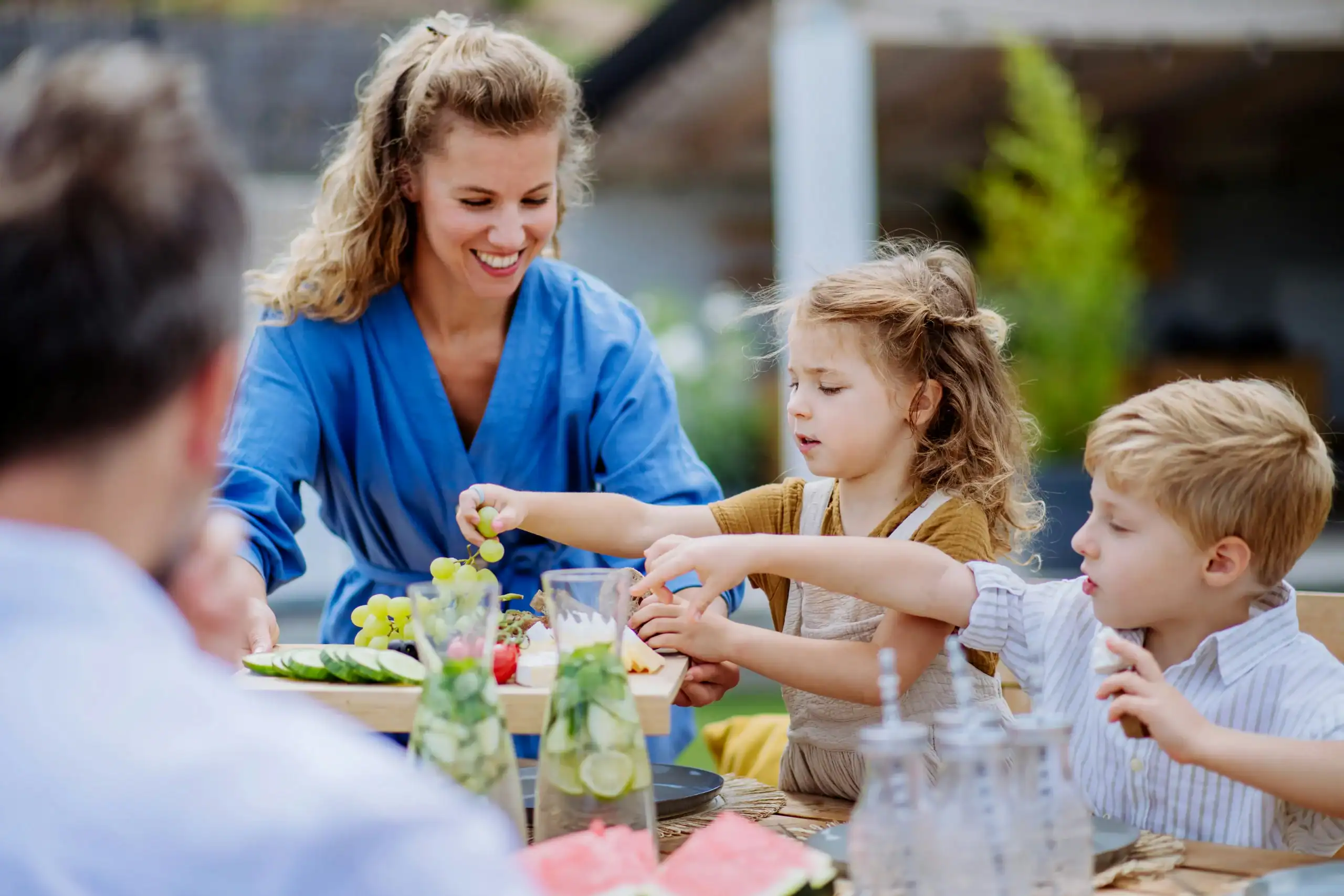 Children at an outdoor table exploring new foods with guidance, managing food texture sensitivity in a social setting Children at an outdoor table exploring new foods with guidance, managing food texture sensitivity in a social setting