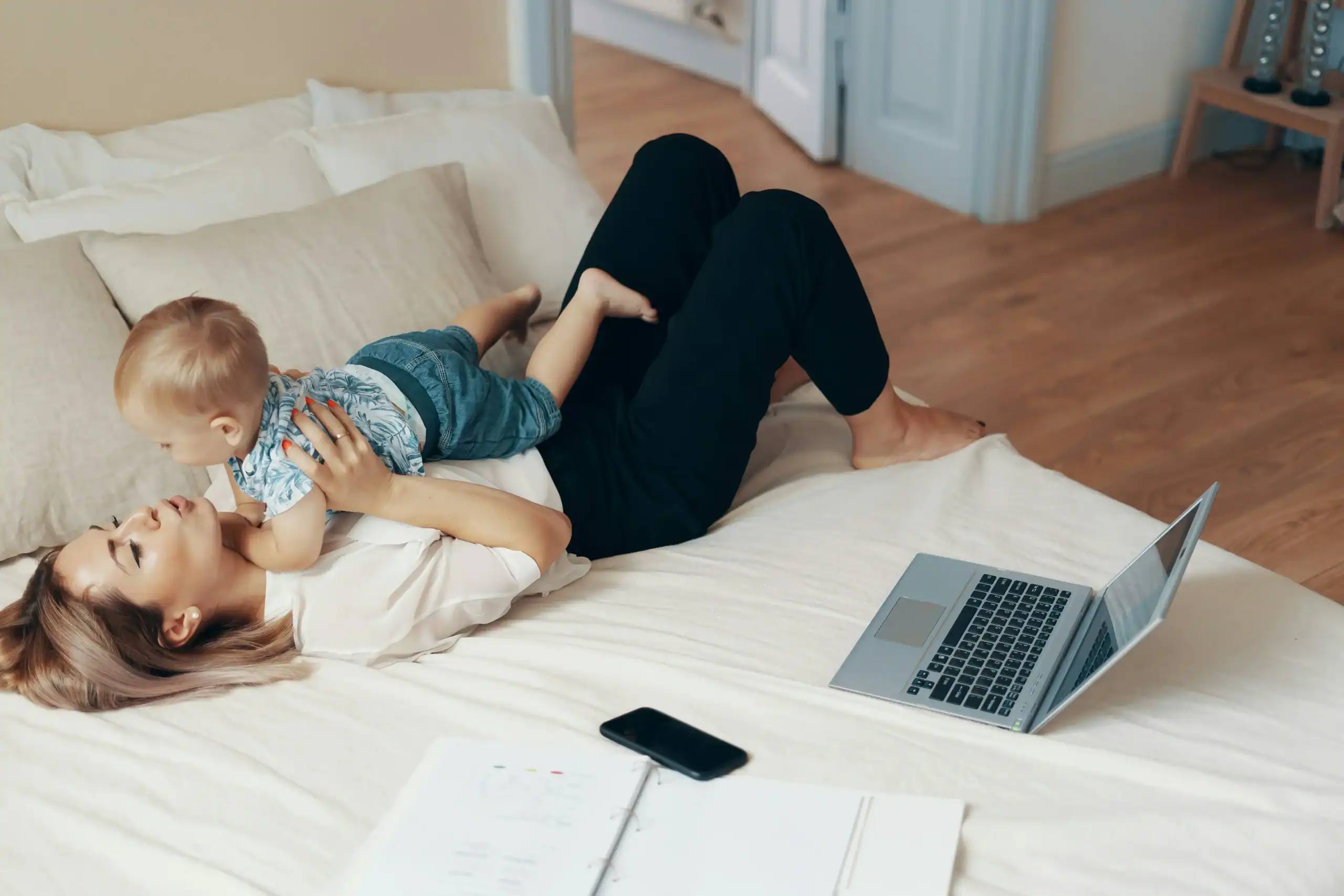 Mother and toddler bonding on the bed next to work materials, portraying the everyday reality of how to balance work and family life Mother and toddler bonding on the bed next to work materials, portraying the everyday reality of how to balance work and family life
