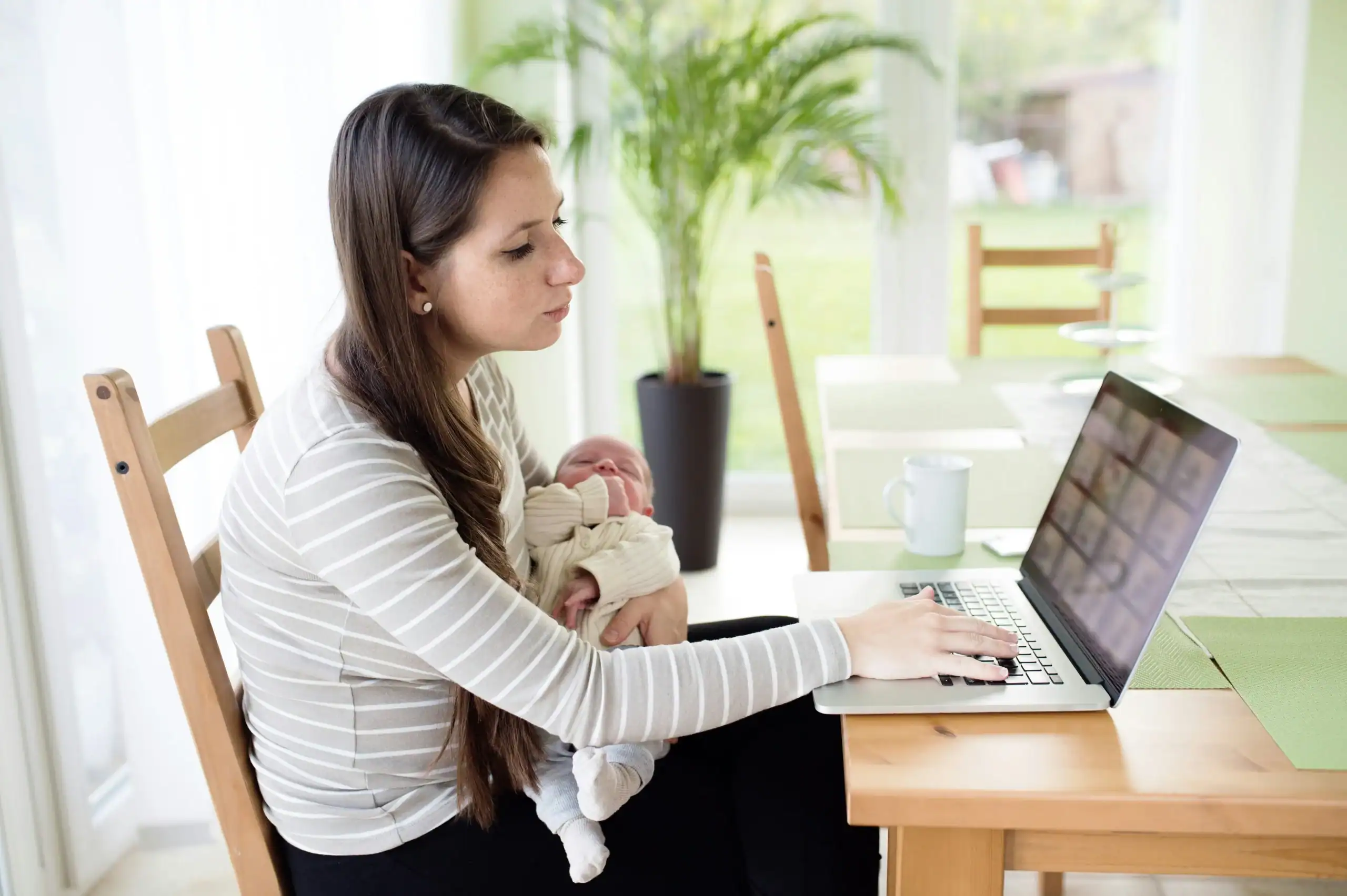 Mother holding baby while working on a laptop, showing how to balance work and family life in a modern home Mother holding baby while working on a laptop, showing how to balance work and family life in a modern home