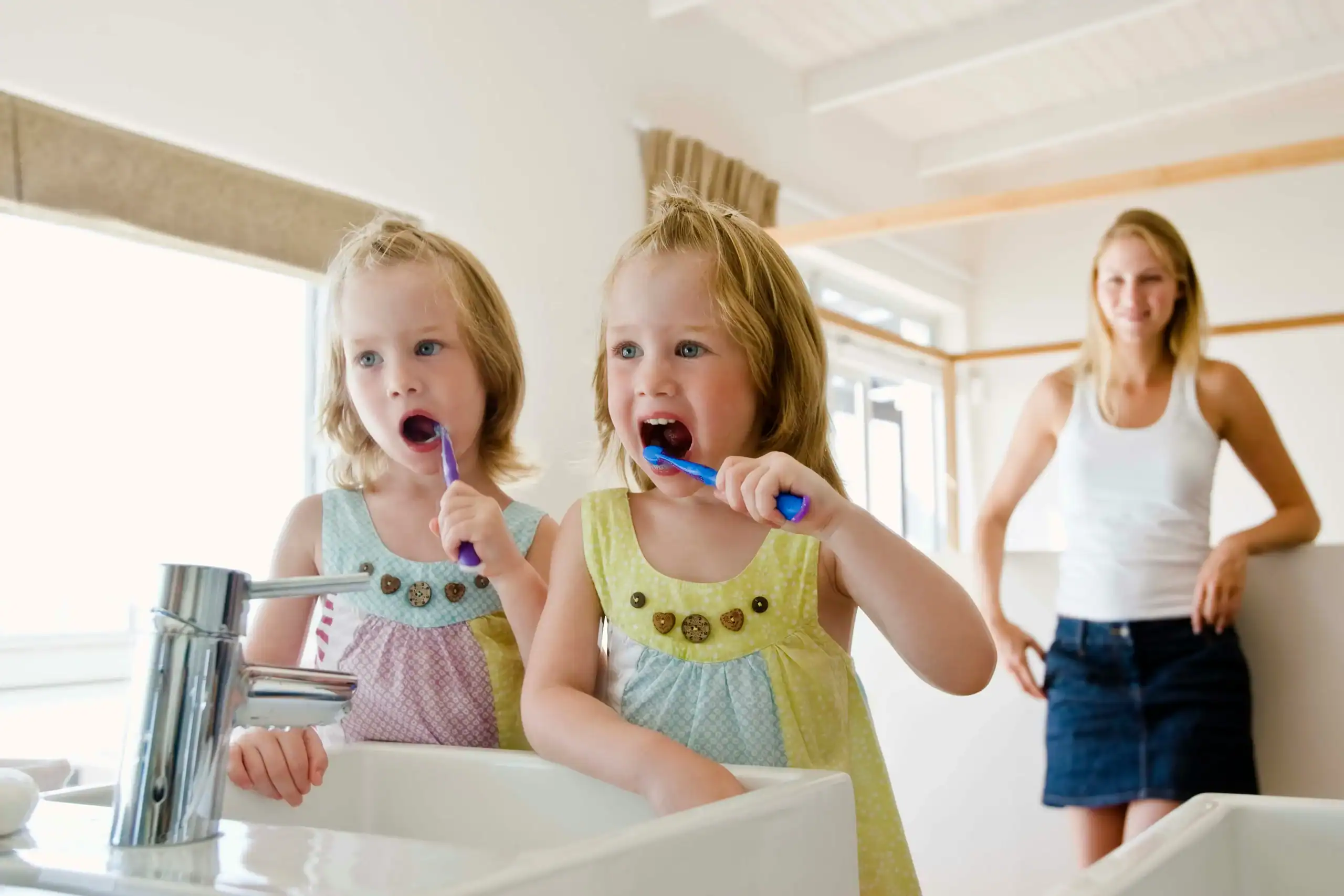 Twin girls brushing teeth with mother nearby, reinforcing autism and hygiene through family support Twin girls brushing teeth with mother nearby, reinforcing autism and hygiene through family support