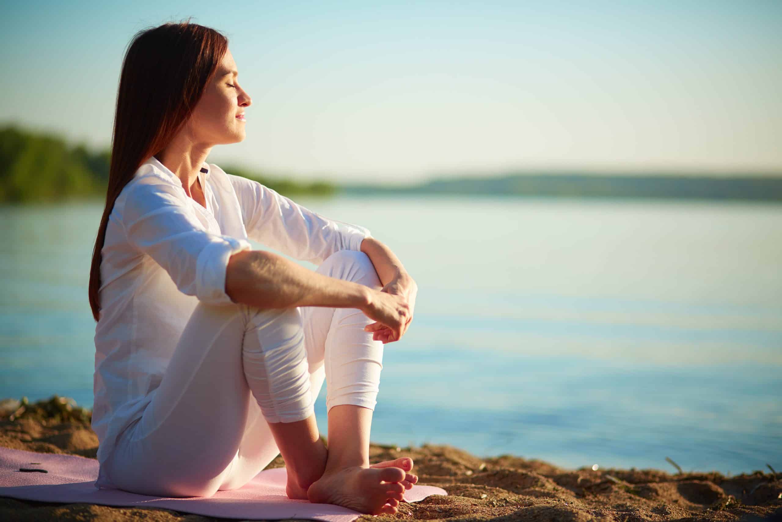 Enjoying life Side view of serene woman sitting on sandy beach against blue sky outdoors