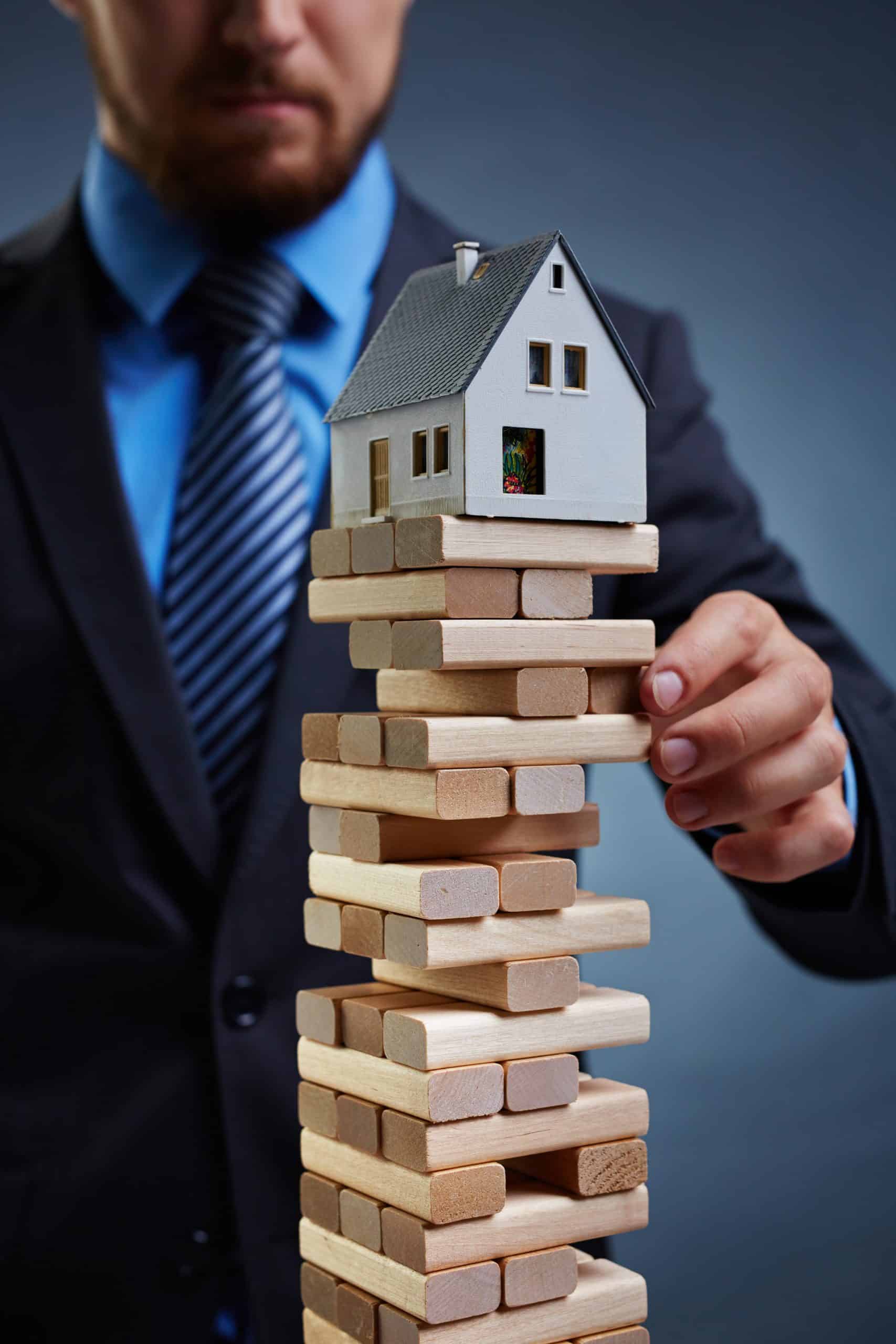 Businessman touching tower from small wooden blocks with house on its top Businessman touching tower from small wooden blocks with house on its top
