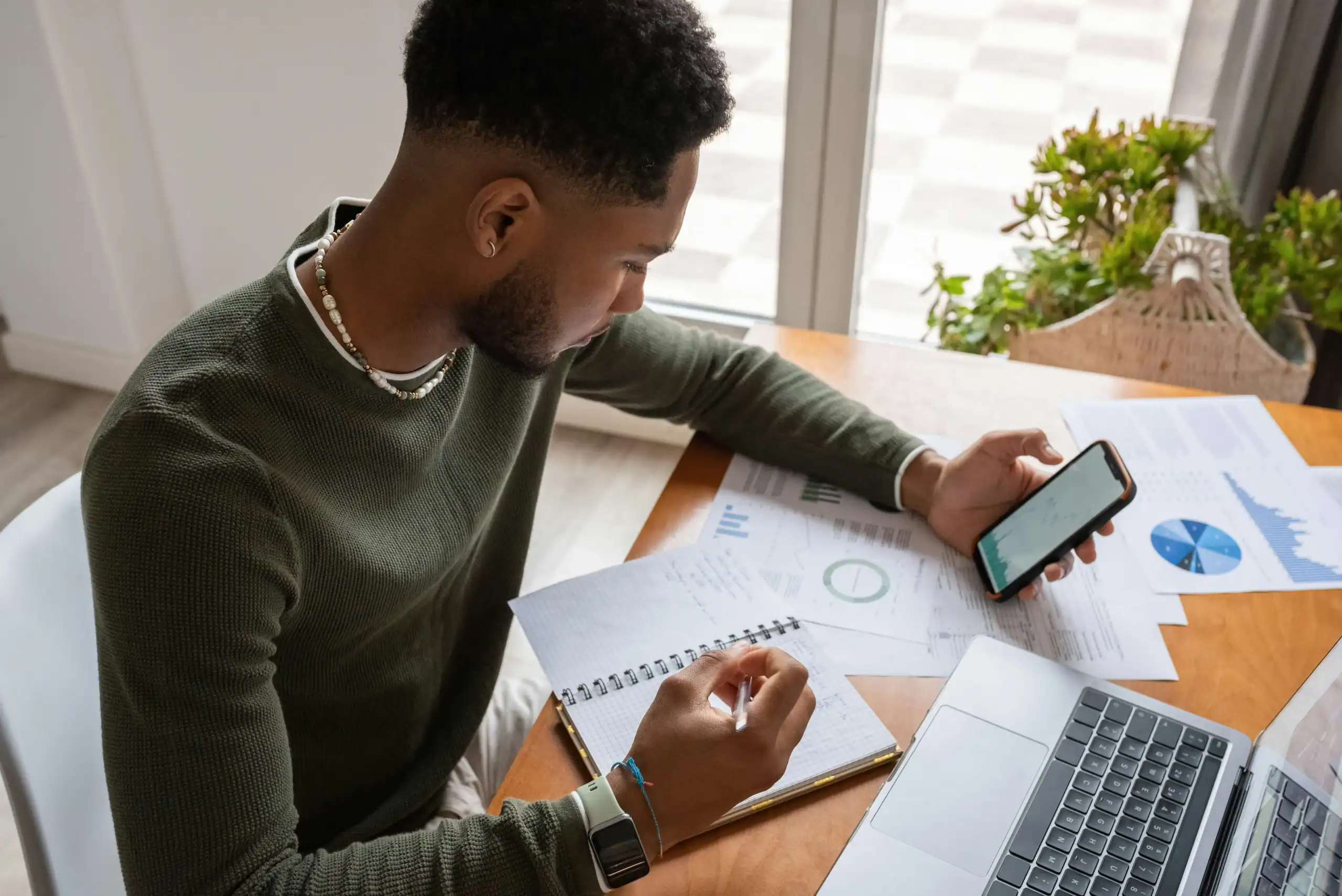 Man reviewing financial charts on phone and notebook for family planning. Man reviewing financial charts on phone and notebook for family planning.