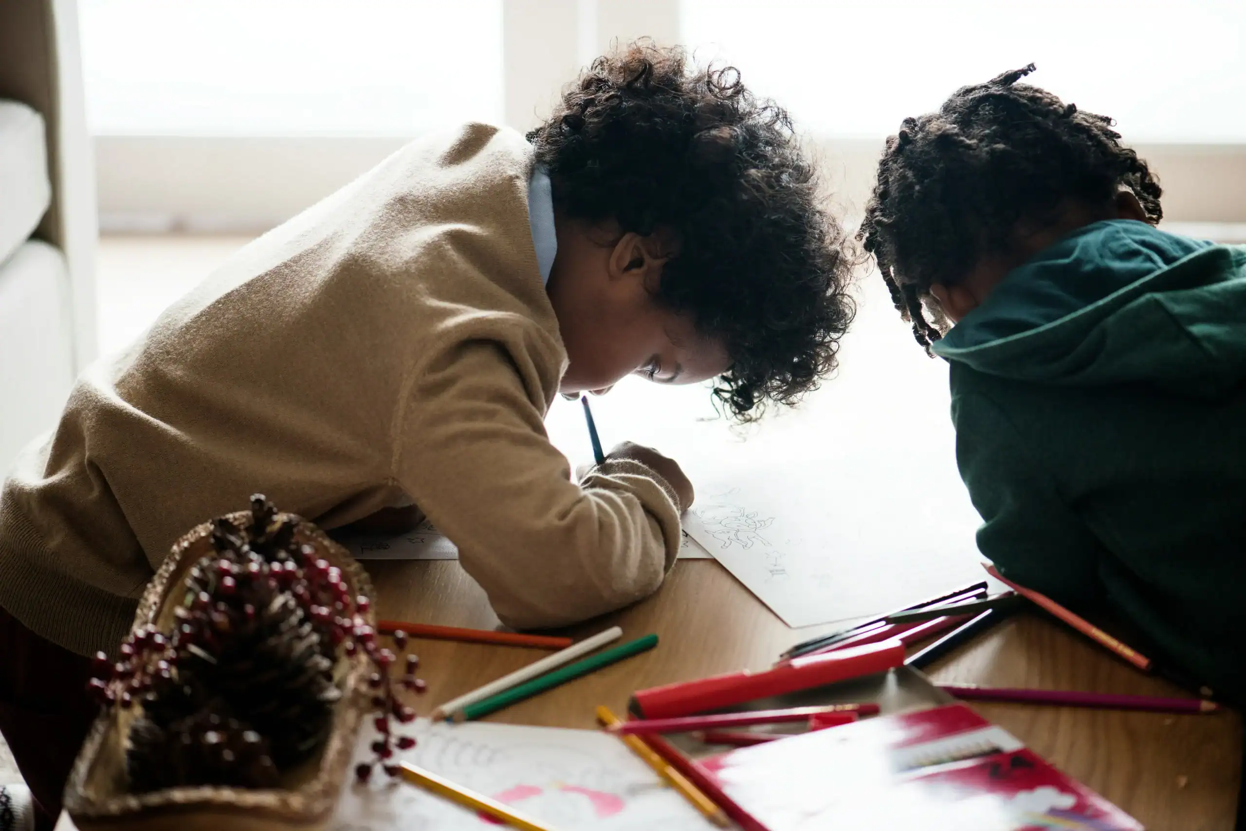 Two children drawing together at a table, illustrating creativity, focus, and autism attachment to objects through play.