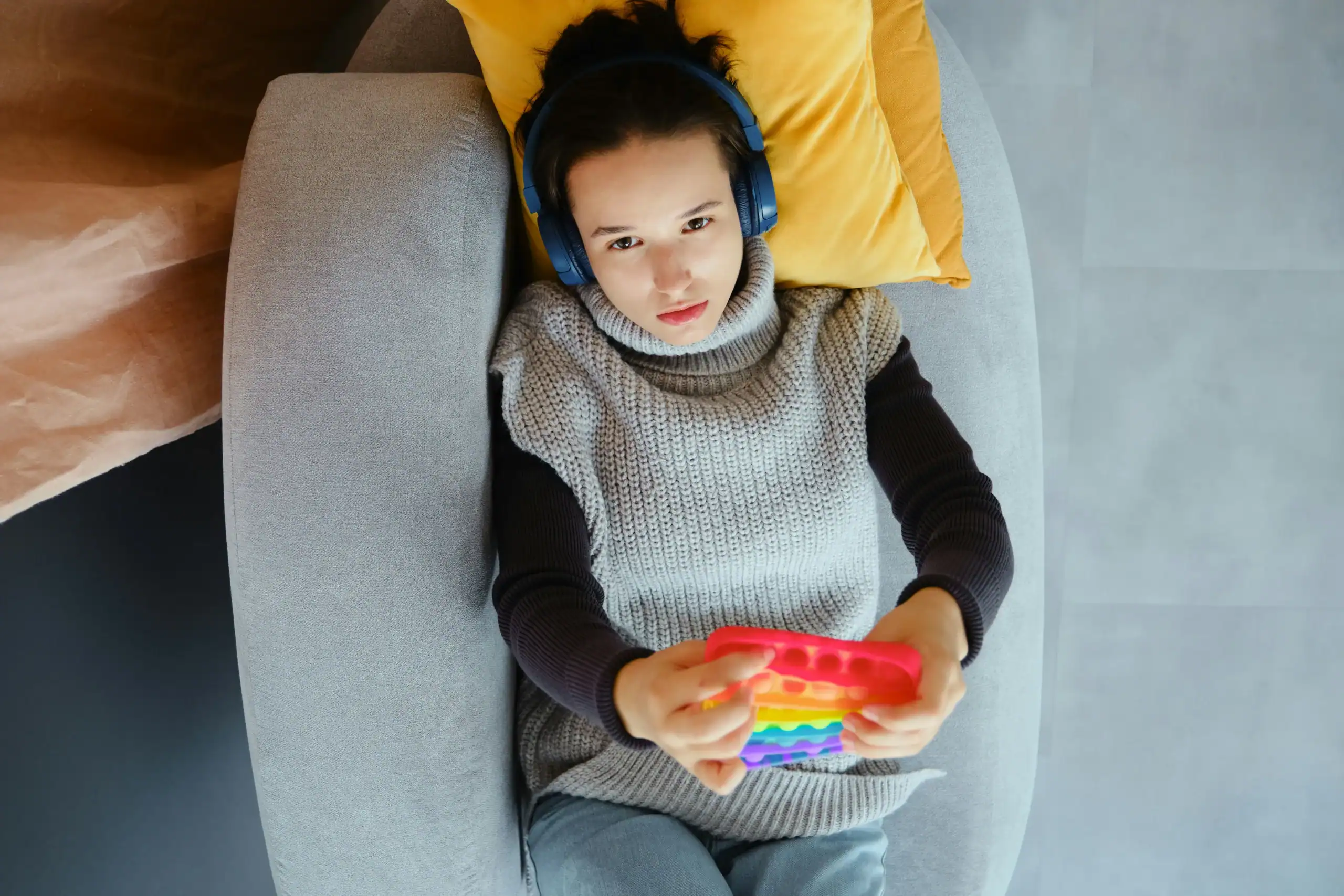Teen using a fidget toy and headphones, popular sensory gifts for autistic adults. Teen using a fidget toy and headphones, popular sensory gifts for autistic adults.